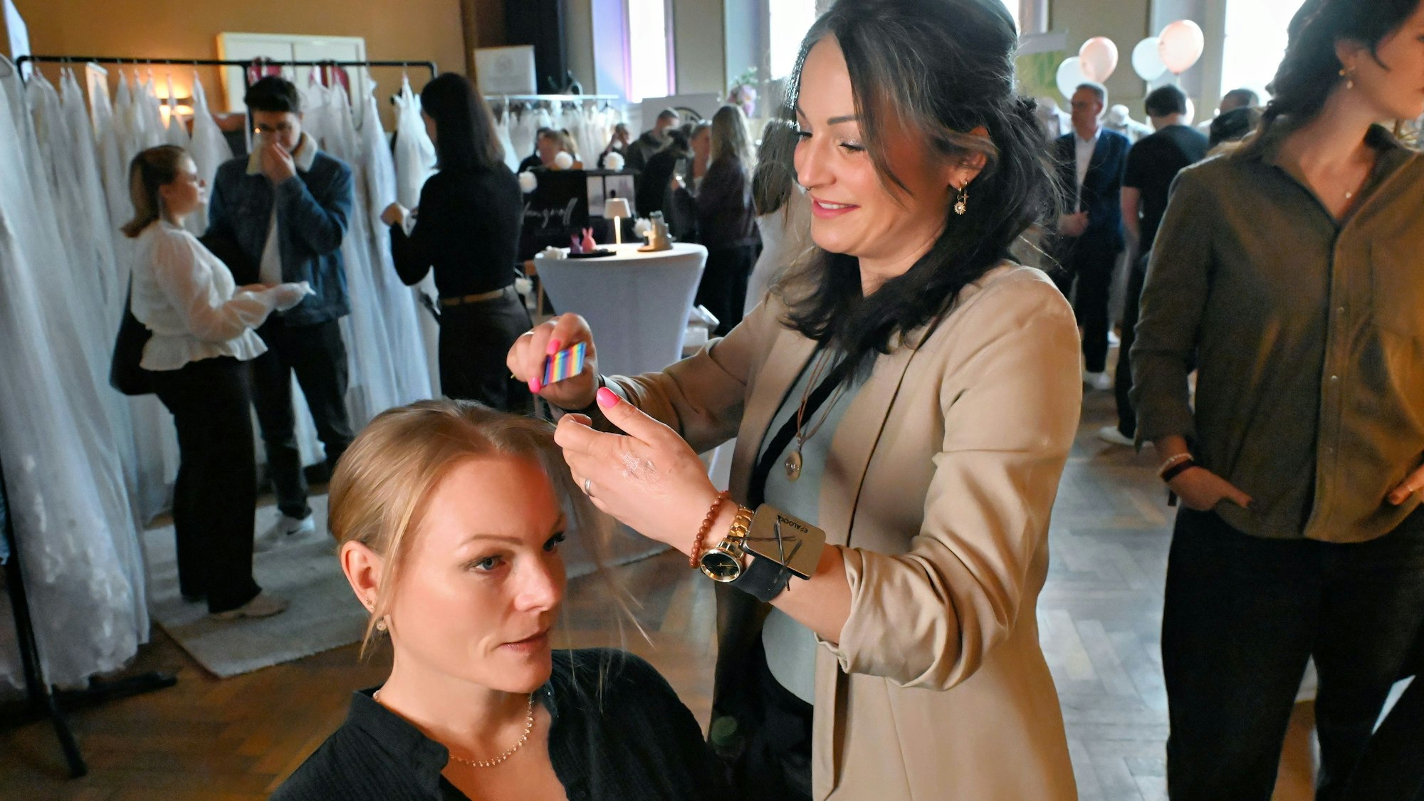 Susi Okon macht einer anderen Frau eine Frisur, im Hintergrund sind Brautkleider zu erkennen.