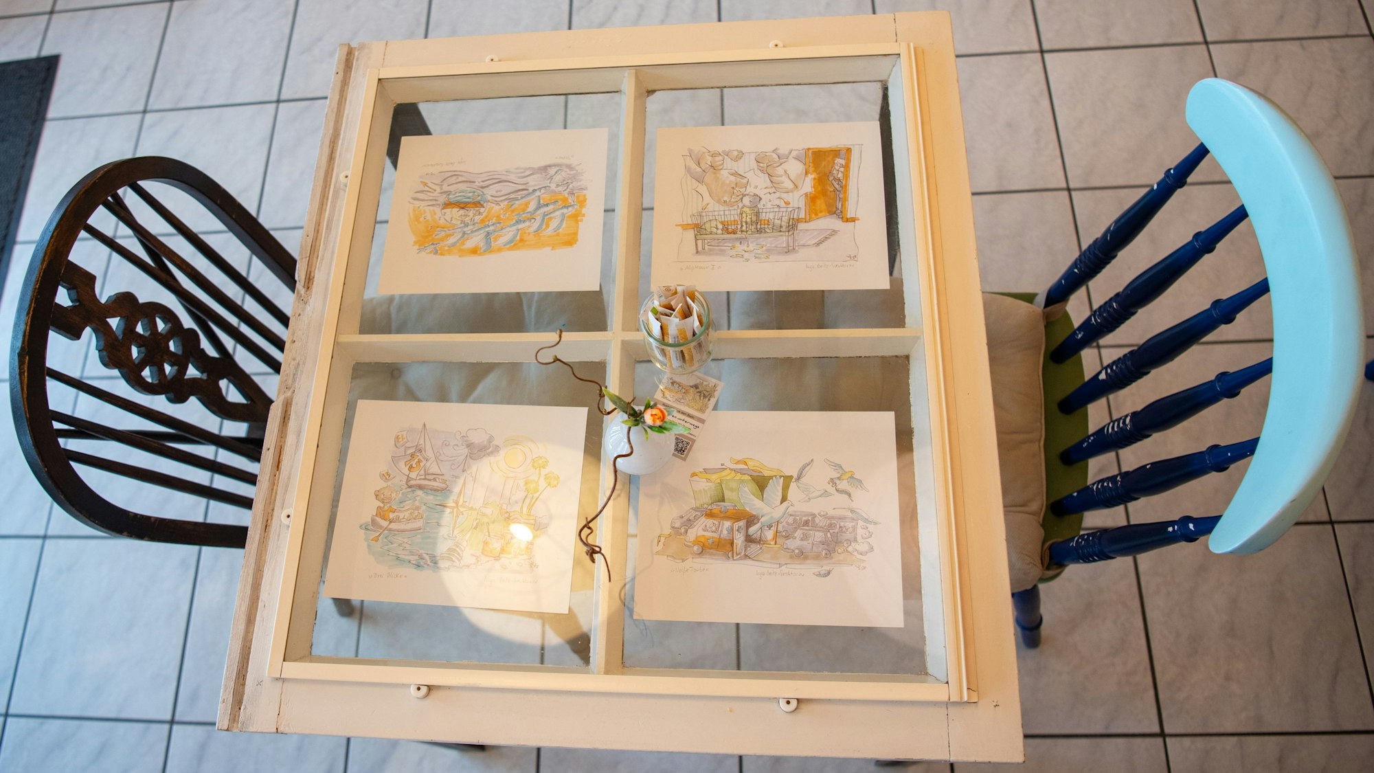 Das Bild zeigt vier Bilder unter einer Tischplatte, die wie ein altes Fenster aussieht. Links und rechts steht jeweils ein Stuhl.