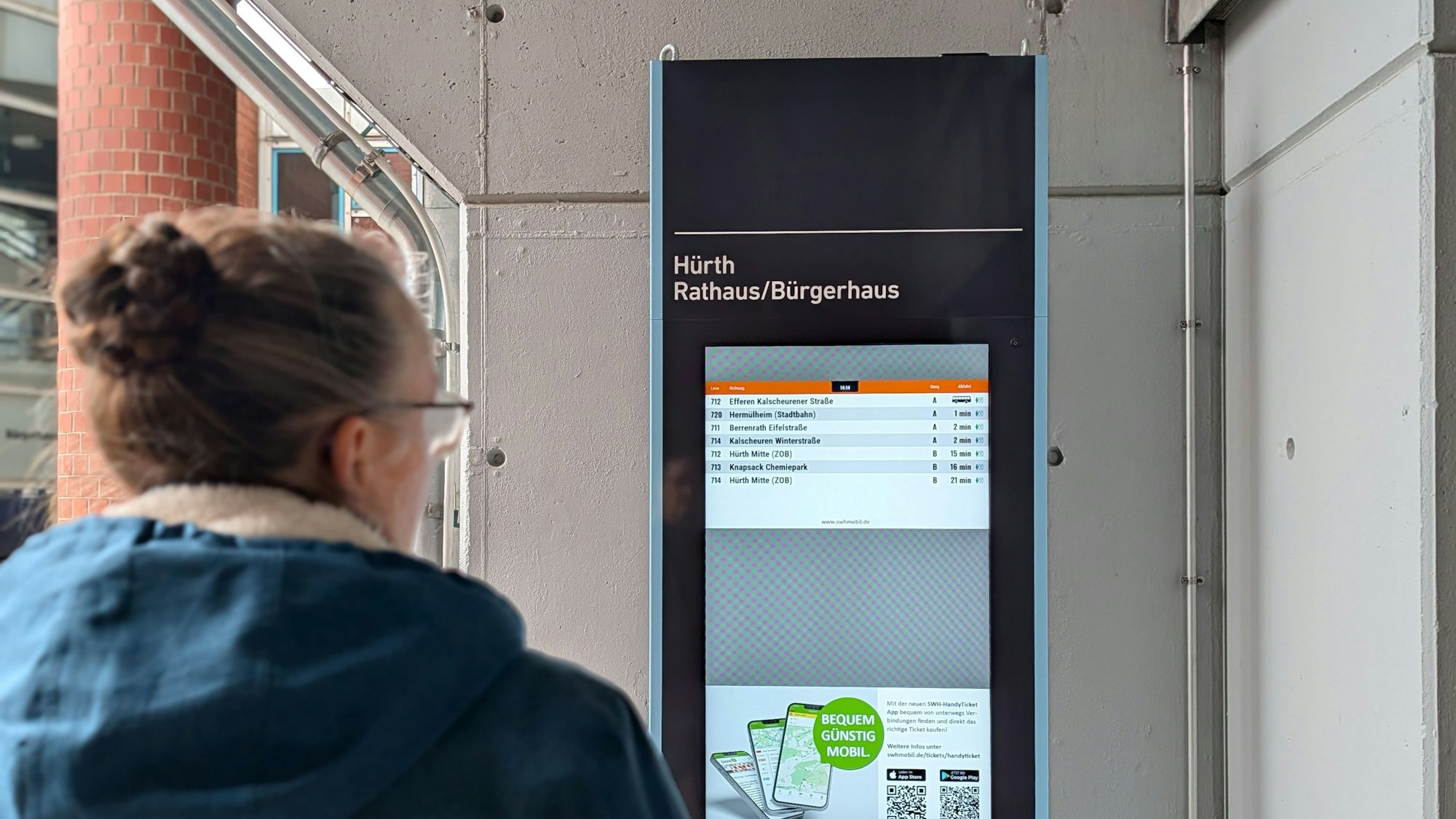 Das Foto zeigt eine Passantin vor der elektronischen Fahrplan-Stele am Rathaus.