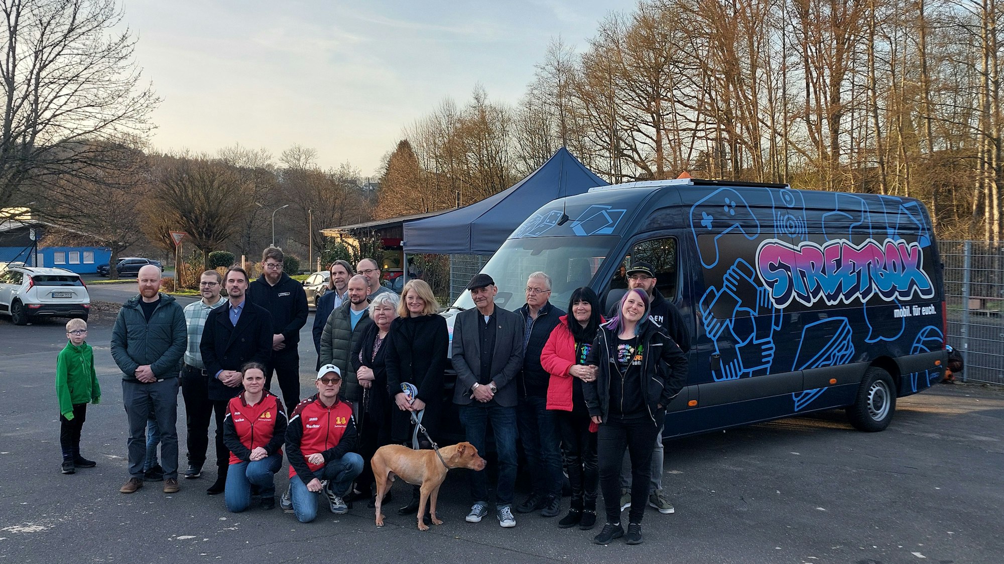Eine Gruppe Menschen steht vor dem Jugendmobil auf einem Parkplatz.