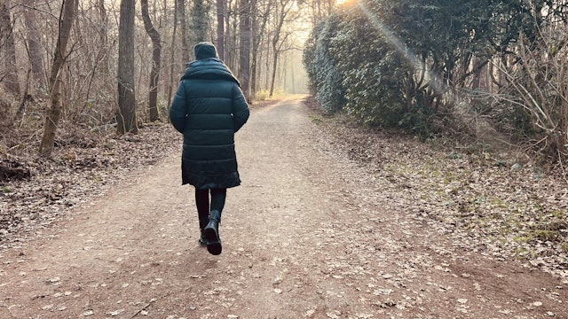 Eine Frau geht mit dem Rücken zur Kamera durch einen Wald.