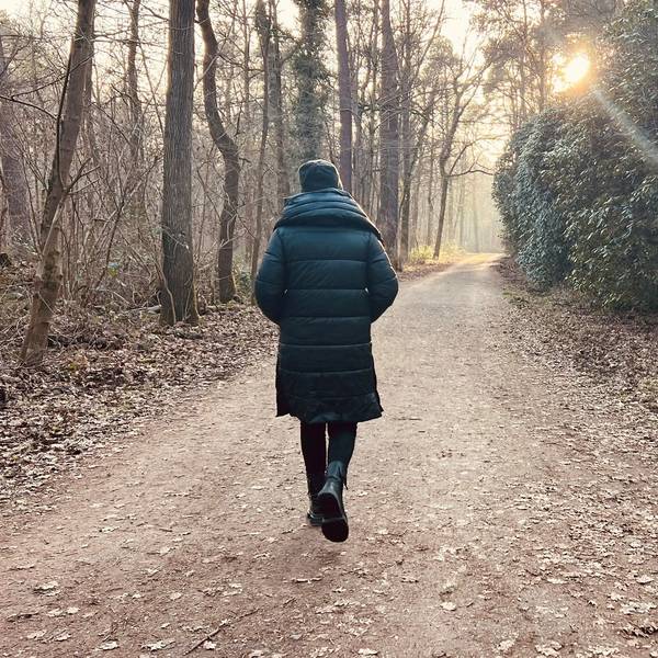 Eine Frau geht mit dem Rücken zur Kamera durch einen Wald.