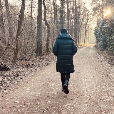 Eine Frau geht mit dem Rücken zur Kamera durch einen Wald.