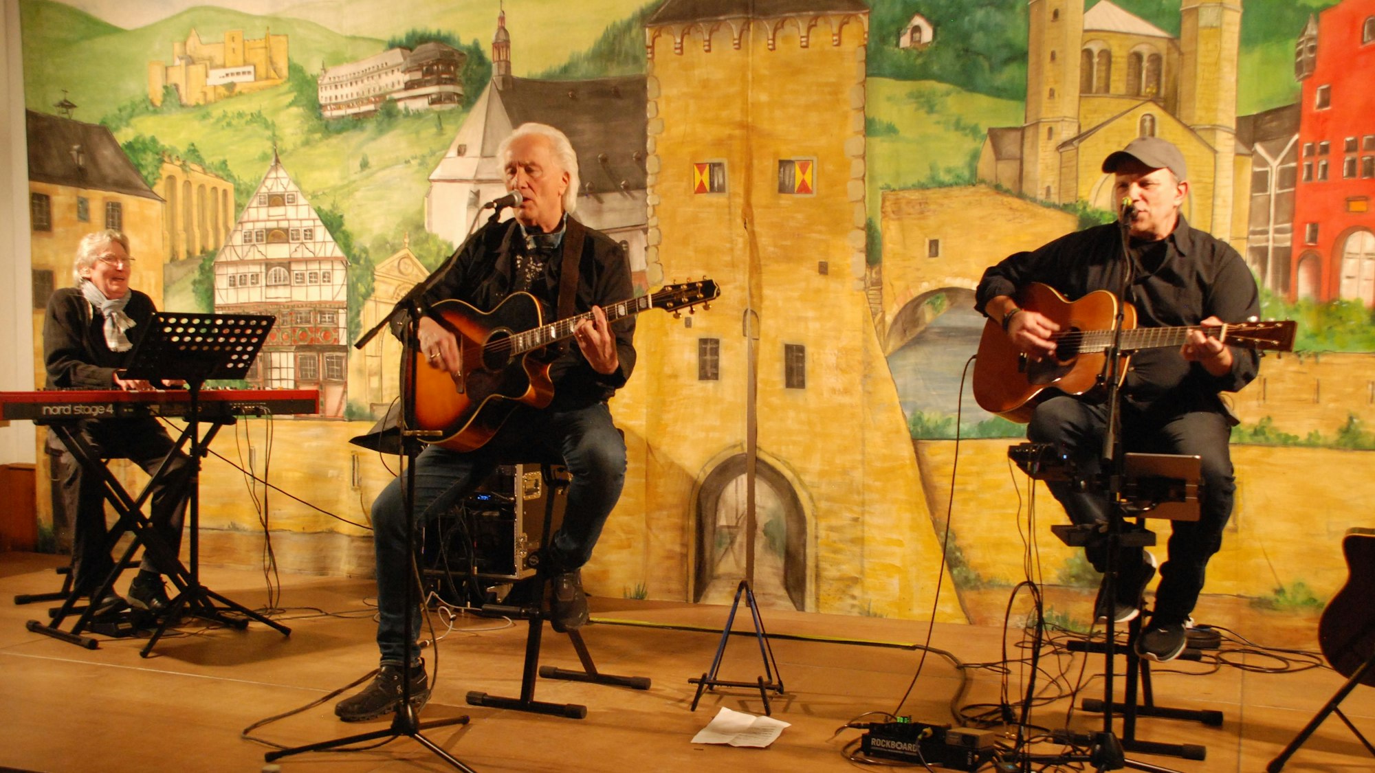 Ady Zehnpfennig spielt auf einem Keyboard, Hannes Schöner und Hermann Heuser spielen Gitarre und singen.