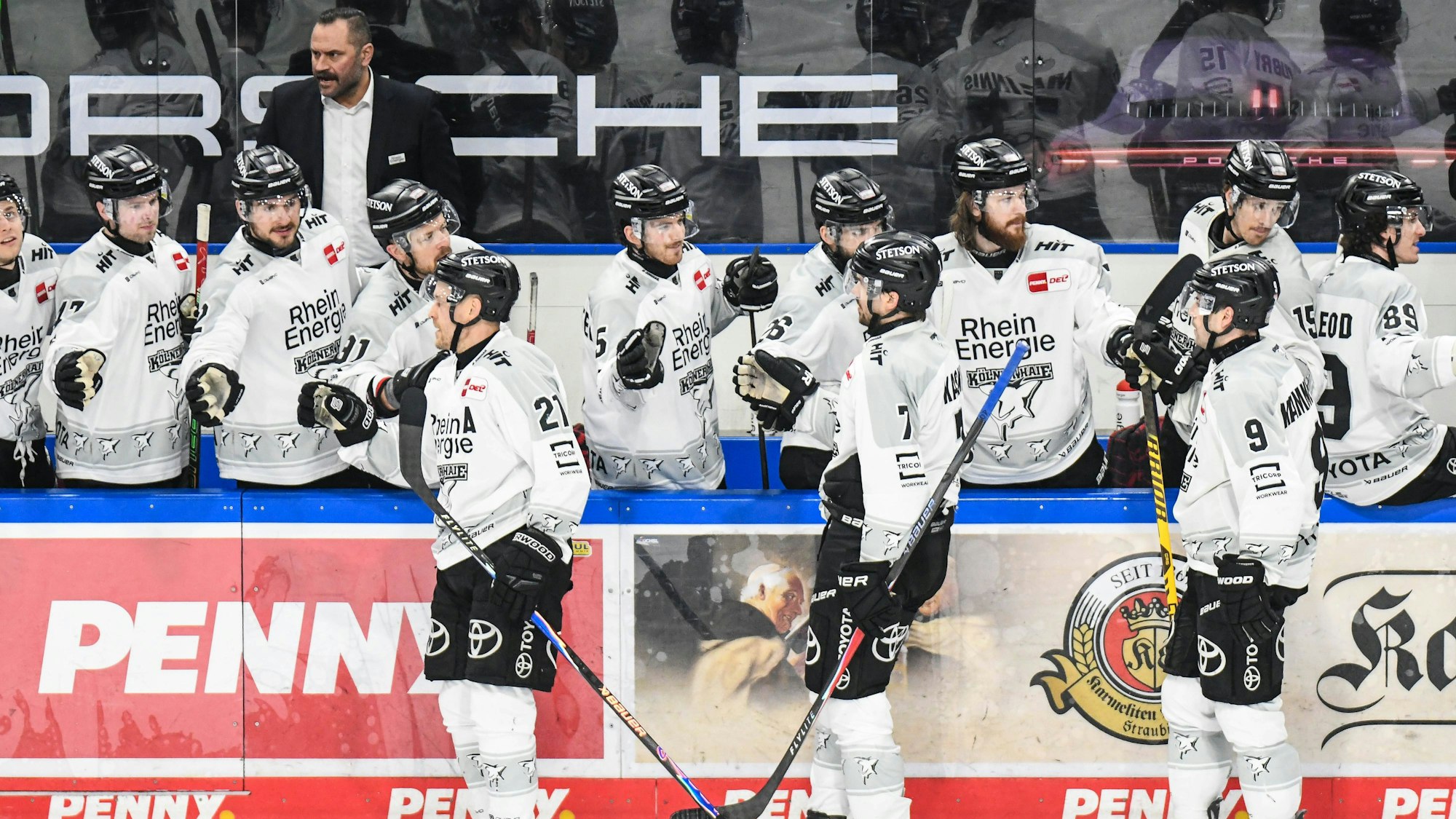 Spieler der Kölner Haie klatschen nach einem Tor mit der Bank ab.