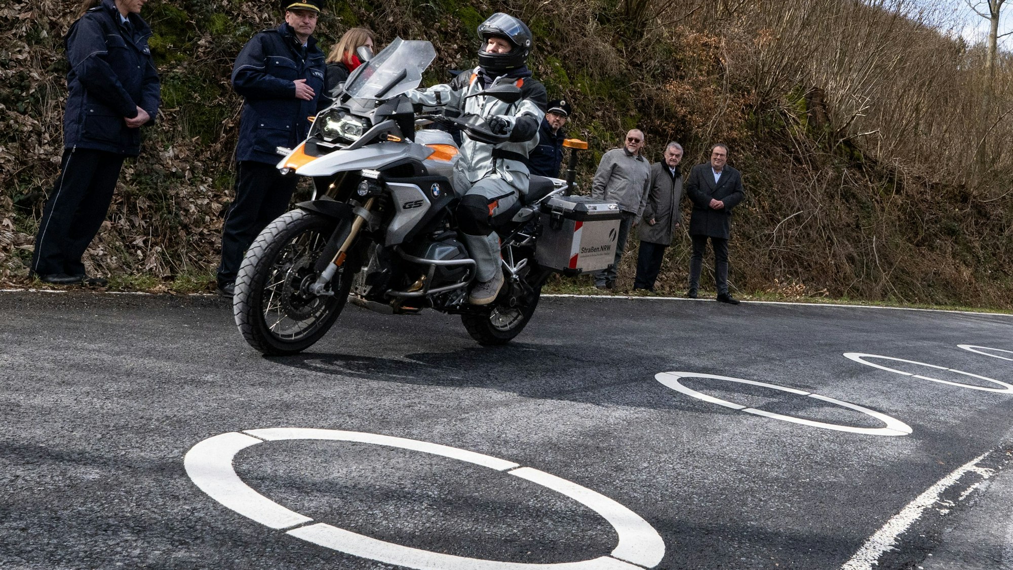 Innenminister Herbert Reul (2.v.r, CDU) und Verkehrsminister Oliver Michael Krischer (r, Bündnis 90/Die Grünen) schauten sich die in Kurven beliebter Motorradstrecken aufgemalten Ellipsen an. Sie sollen verhindern, dass Motorradfahrer die Kurven schneiden.