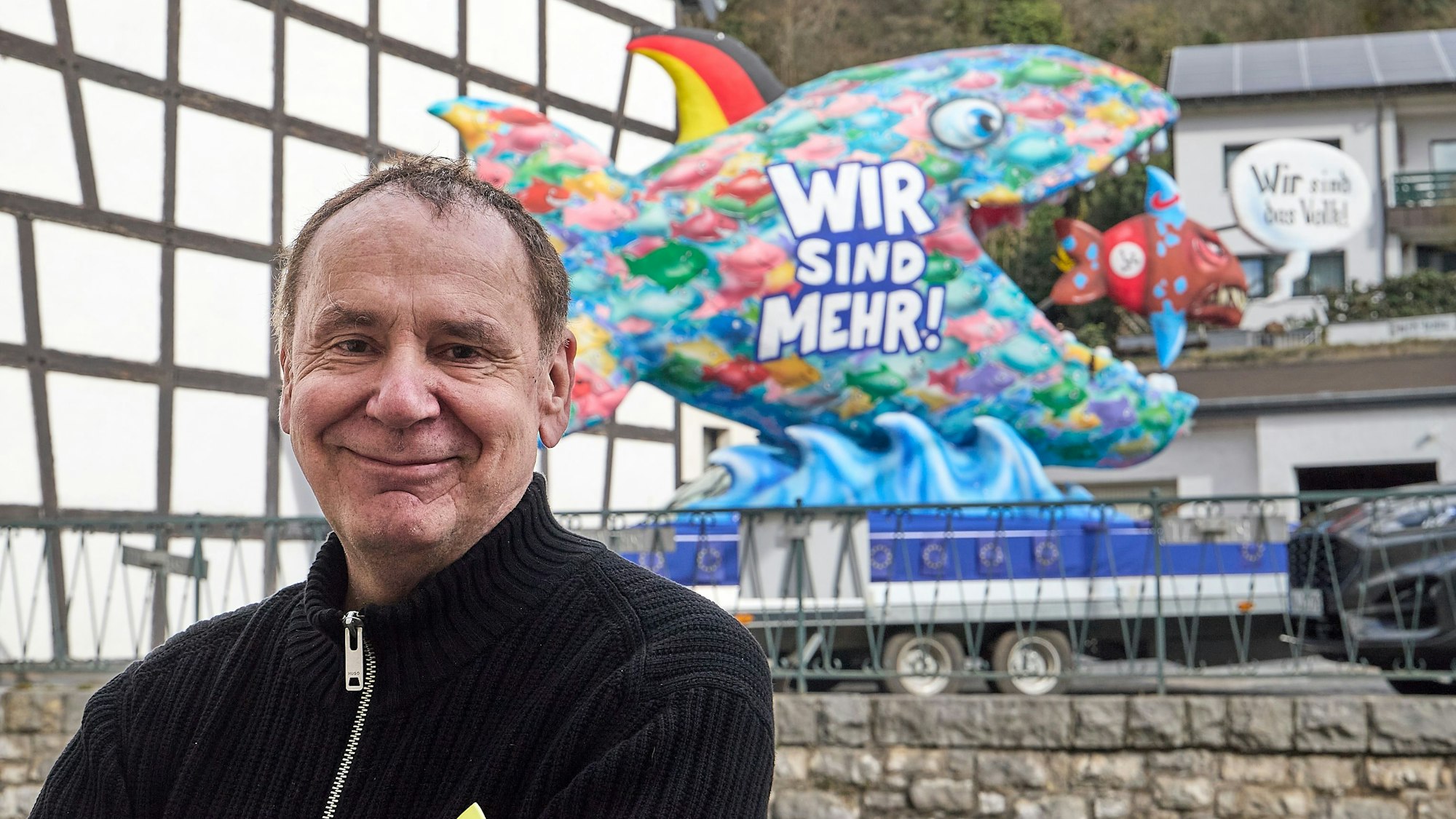 Jacques Tilly stehrt vor einem seiner Karnevalswagen. Der zeigt einen großen Fisch, der einen kleinen verschluckt.