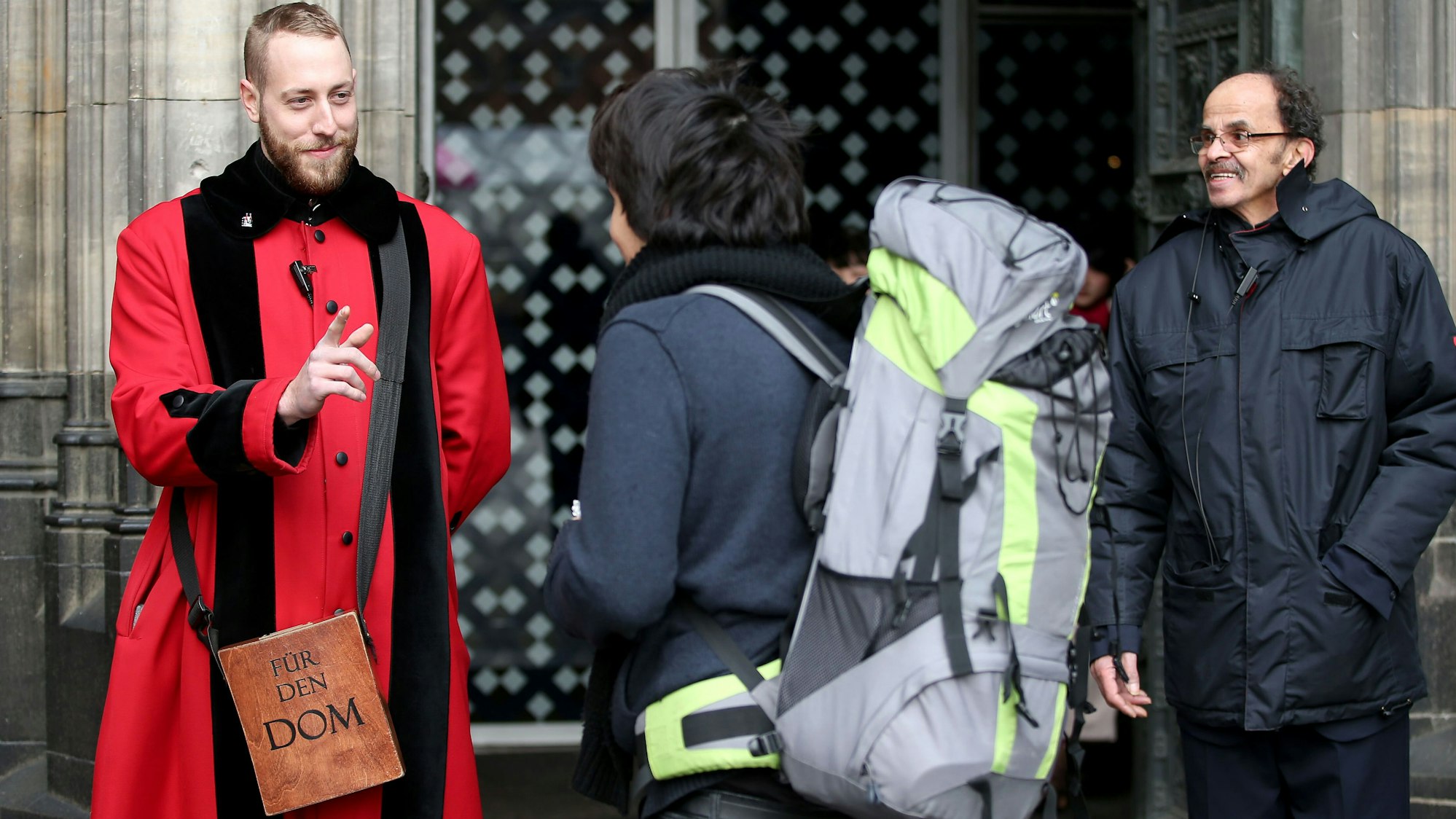 Archivfoto: Ein Domschweizer (links) spricht mit einem Touristen vor dem Eingang des Kölner Doms. Ab der zweiten Jahreshälfte 2026 sollen Besucher mit touristischem Interesse ein Eintrittsgeld zahlen