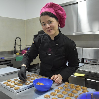 Zu sehen ist eine Frau in ihrer Schokoladenmanufaktur, auf dem Tisch liegen verschiedene Pralinen.