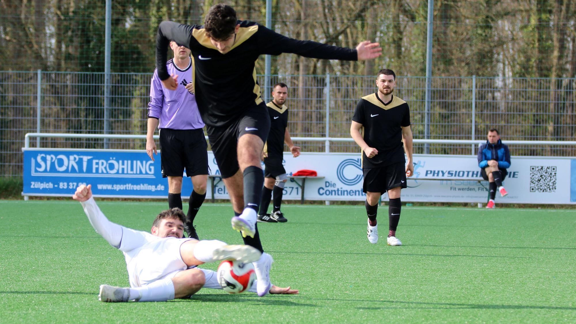 Ein Fußballer grätscht einem anderen den Ball vom Fuß.