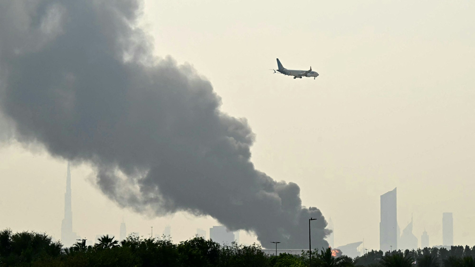Ein Flugzeug fliegt am an Rauchwolken vorbei, die von einem Brand in der Nähe des Dubai International Airport in Dubai aufsteigen. (Symbolbild)