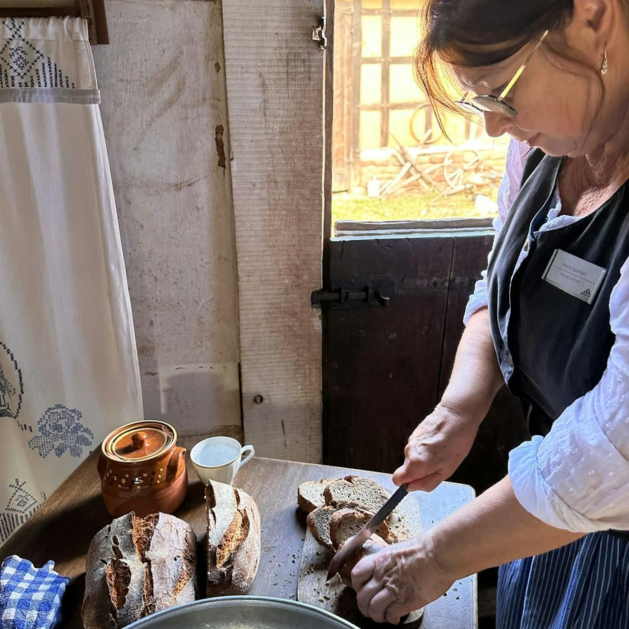 Eine Frau schneidet Brot in traditioneller Bekleidung.