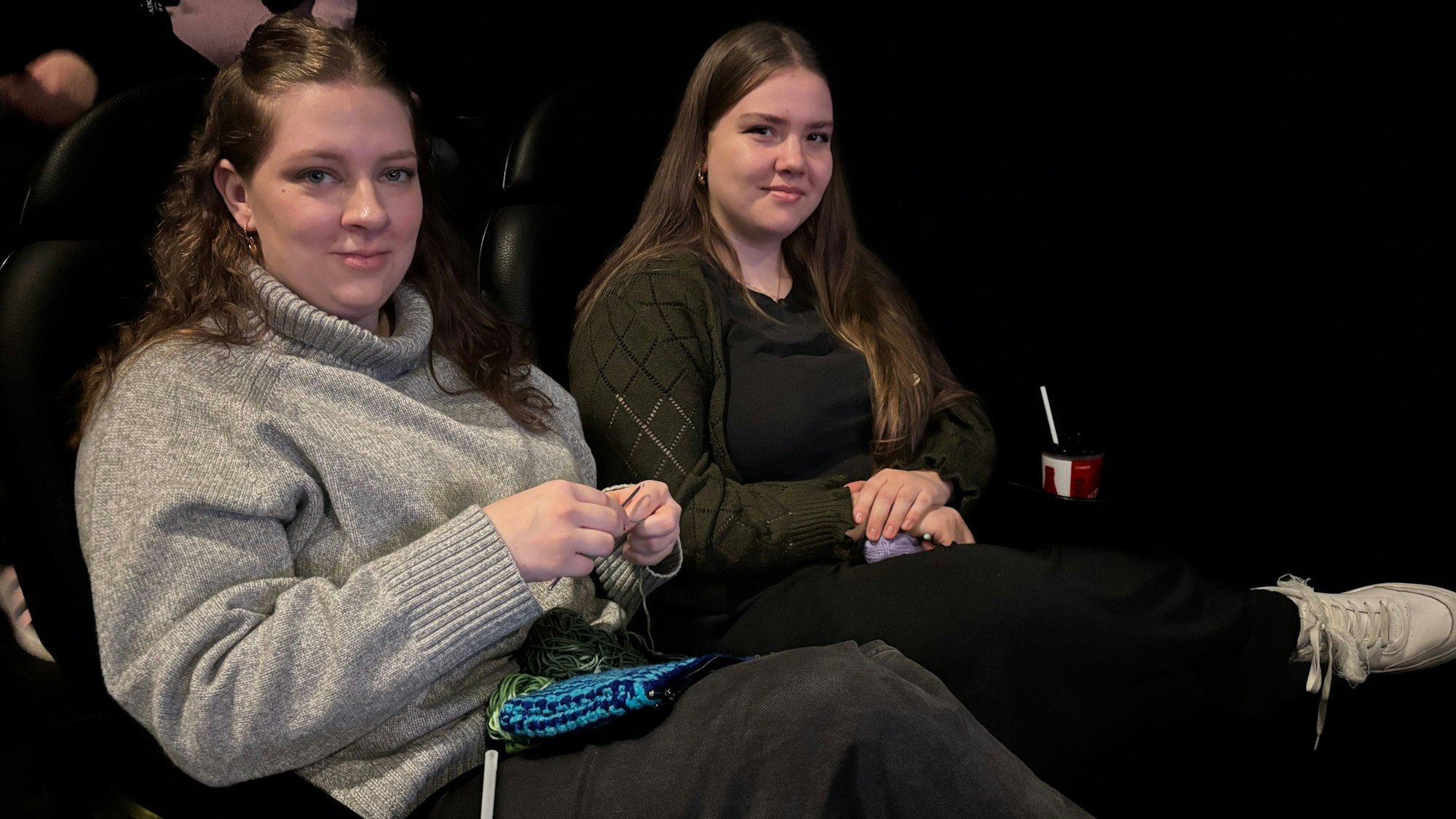 Zwei junge Frauen sitzen im Kino und blicken in die Kamera.