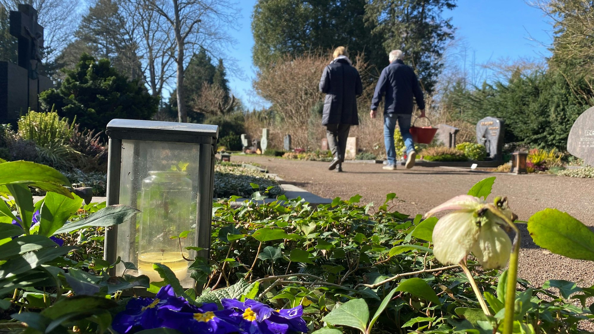 Zu sehen sind Gräber auf dem Brühler Südfriedhof sowie zwei Friedhofsbesucher.