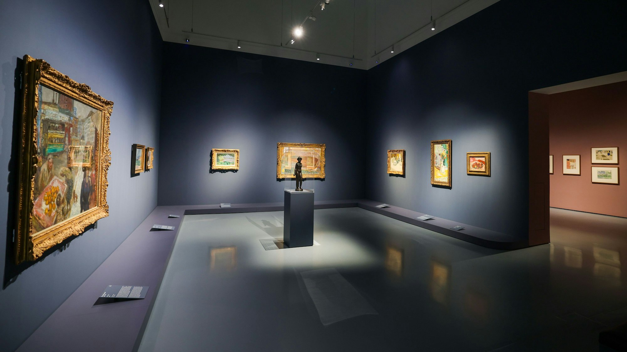 In einem Raum hängen Gemälde an blauen Wänden.