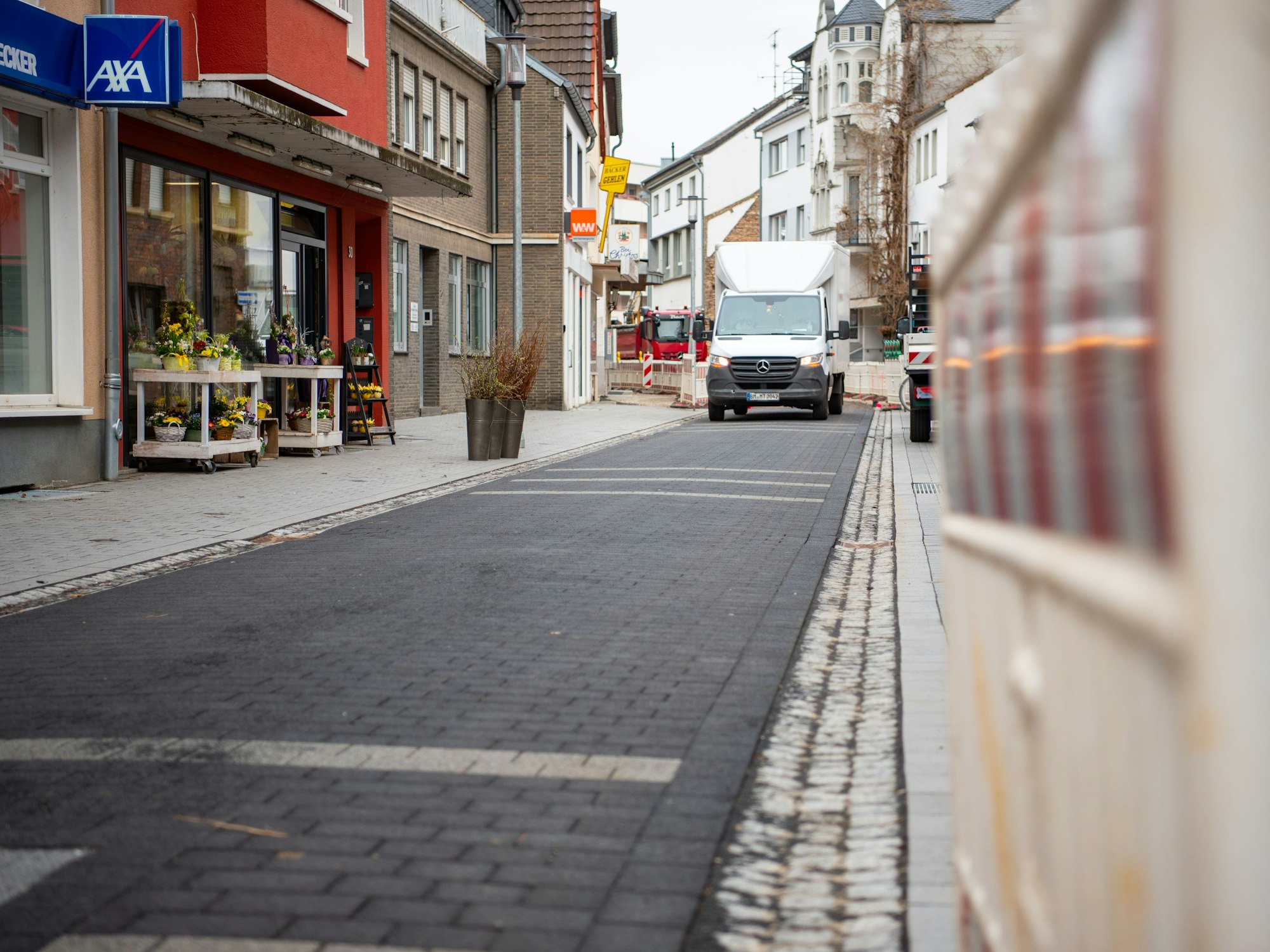 Das Bild zeigt eine frisch gepflasterte Straße, rechts ist eine Warnbake zu erkennen, links ein Blumenladen.