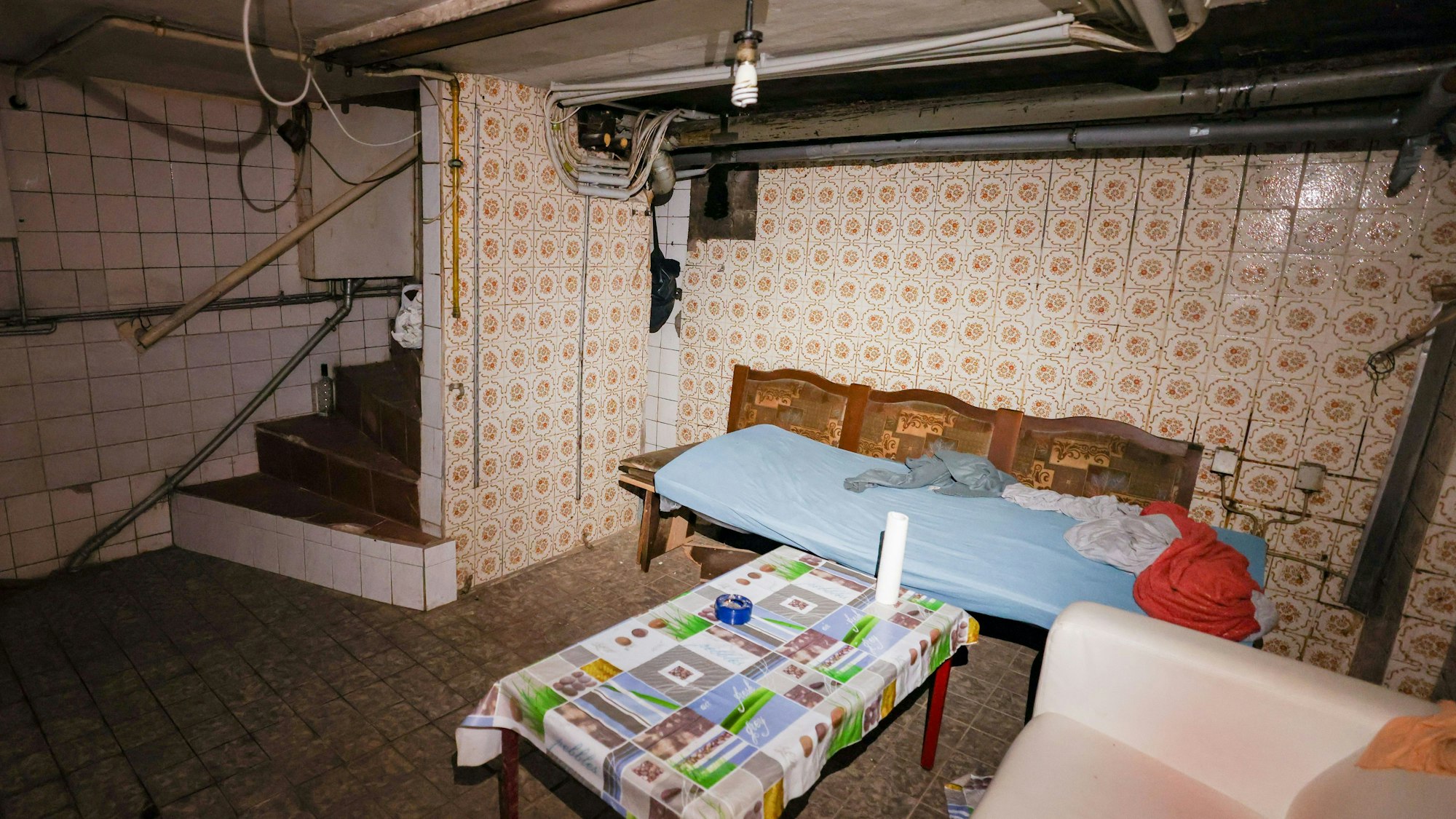 In einem Kellerraum einer Schrottimmobilie befinden sich mehrere provisorische Schlafplätze und ein Holztisch. In Nordrhein-Westfalen soll künftig schärfer gegen Zweckentfremdung von Wohnraum, ausbeuterische Unterbringung Beschäftigter und Schrottimmobilien vorgegangen werden.