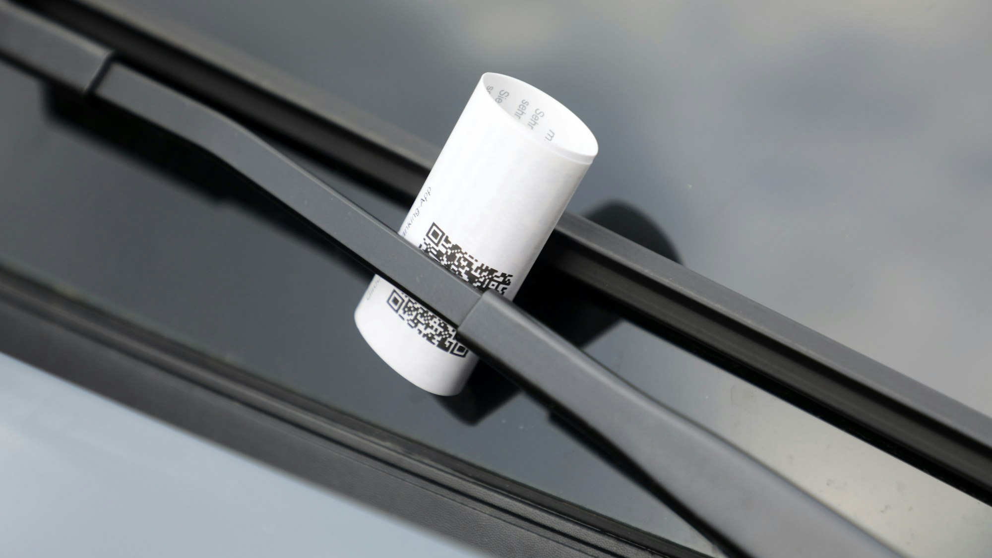 Ein Strafzettel ist unter einen Scheibenwischer an einer Windschutzscheibe gesteckt.