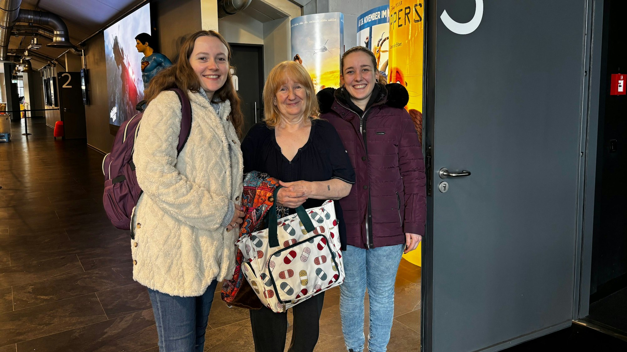 Die drei Frauen stehen im Foyer des Kinos und lächeln in die Kamera. Sybille Klockner hält eine Häkeltasche in der Hand.