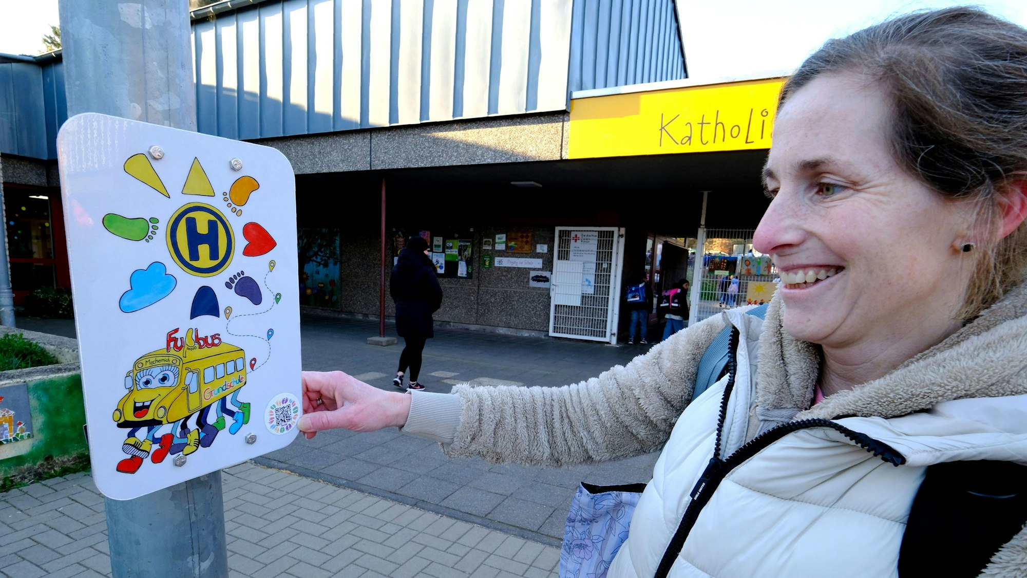 Eine Frau steht an der Grundschule in Mechernich an einem Schild, das die Haltestelle des Fußbusses kennzeichnet.