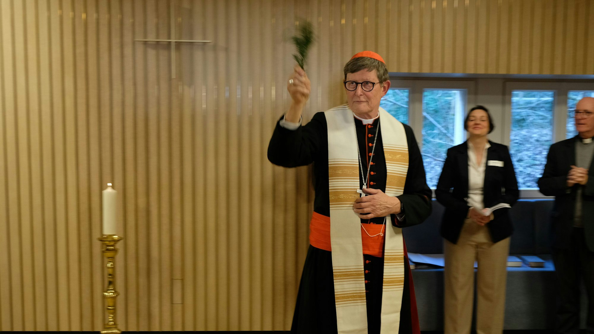 Ein Kardinal segnet einen Raum mit einem grünen Palmzweig.