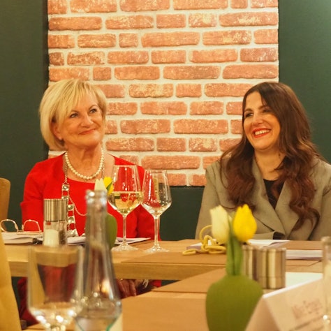 Bernadette Hein (l.) und Judith Kneuttinger sitzen an einem Tisch mit Weingläsern und Blumen darauf.