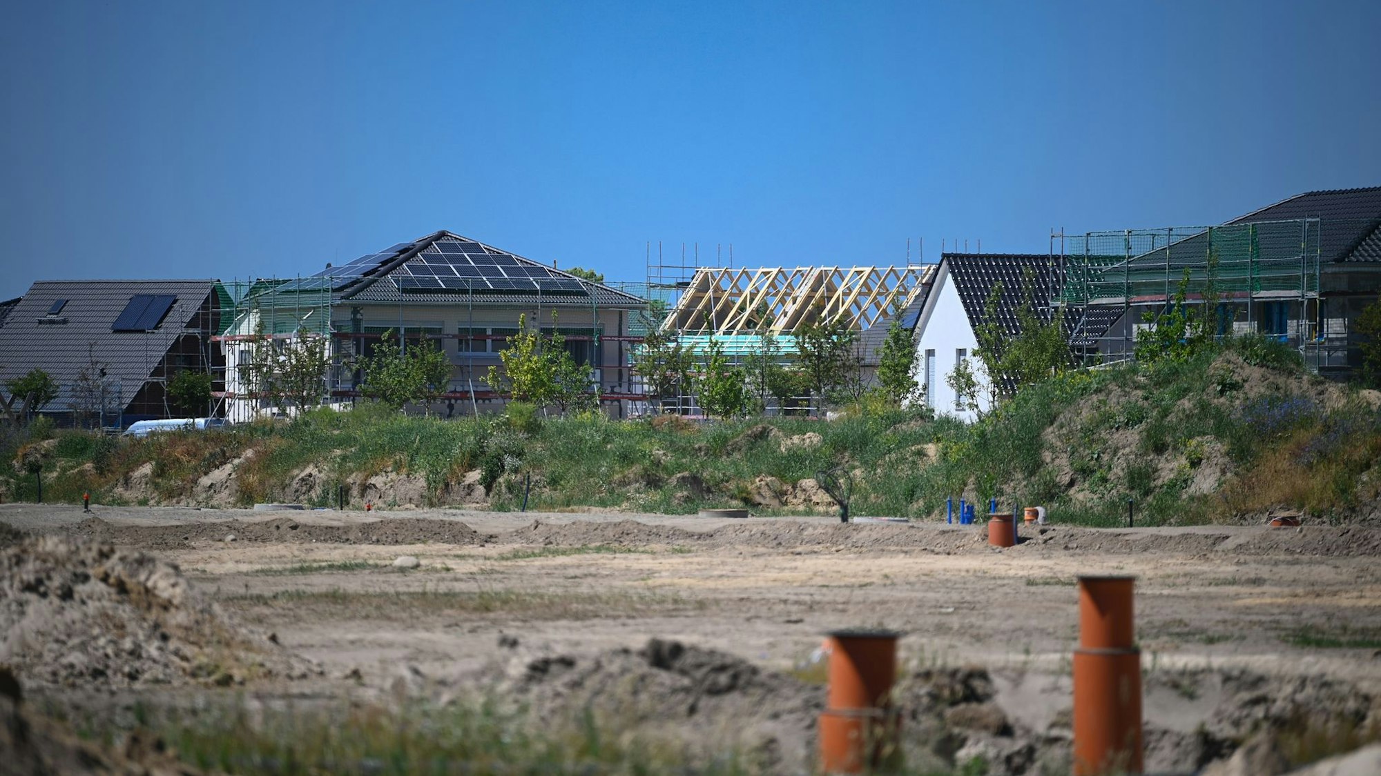 Einfamilienhäuser und Rohbauten stehen hinter einer Baustelle