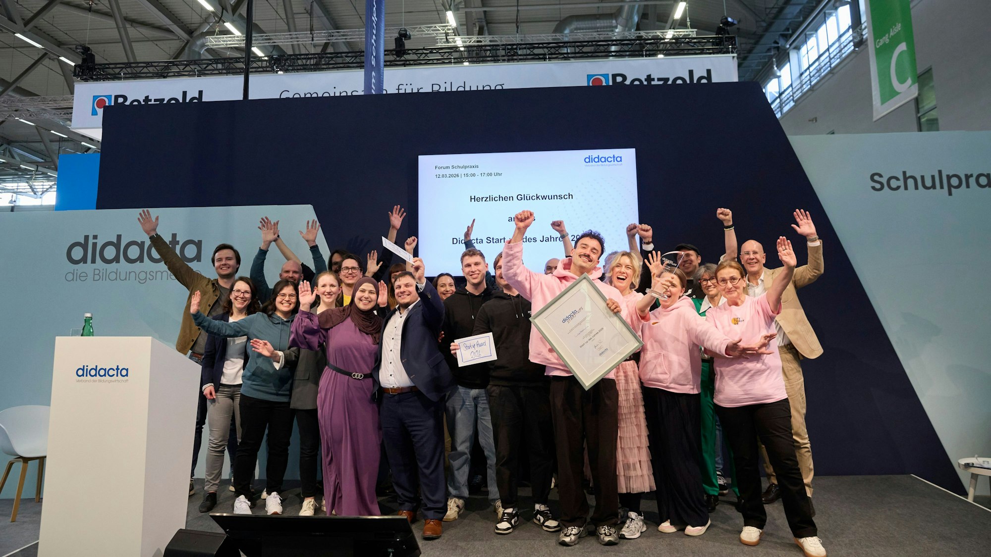 Eine Gruppe von Menschen jubelt in die Kamera. Ein Mann vorne hält ein gerahmtes Bild in der Hand.