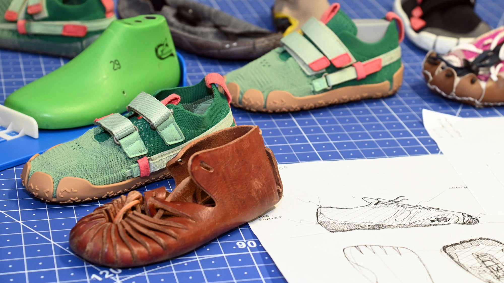 Auf einer Arbeitsfläche stehen die grünen Schuhe von Sizeless, daneben lederne Römersandalen, Prototypen und Entwurfsskizzen.