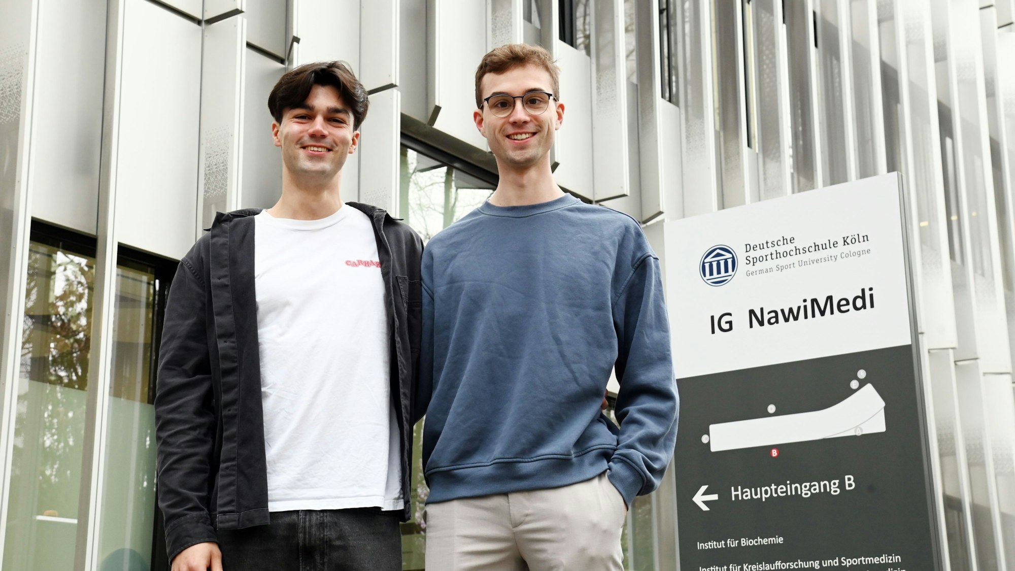 Alexander Schemel und Leander Peters stehen vor dem NawiMedi-Institutsgebäude der Deutschen Sporthochschule Köln.