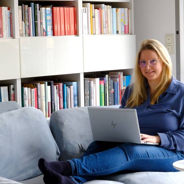 Yvonne Kraus aus Eicks, die als Buchcoach arbeitet, sitzt mit ihrem Laptop auf dem Sofa vor einem Bücherregal.