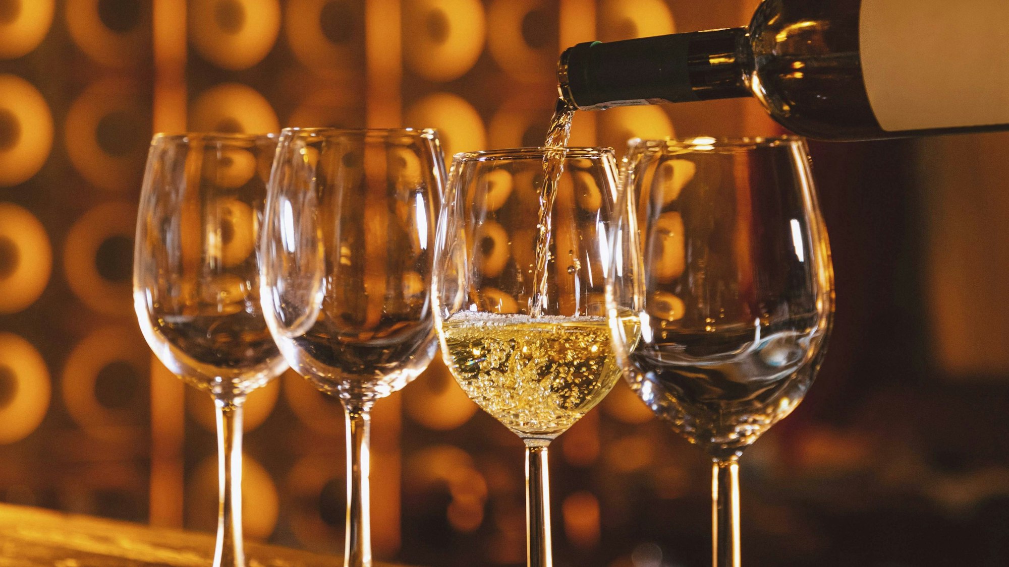 Barkeeper gießt Weißwein aus einer Flasche in eine Reihe von Gläsern auf einem Bartresen mit einem unscharfen Restaurant Hintergrund.