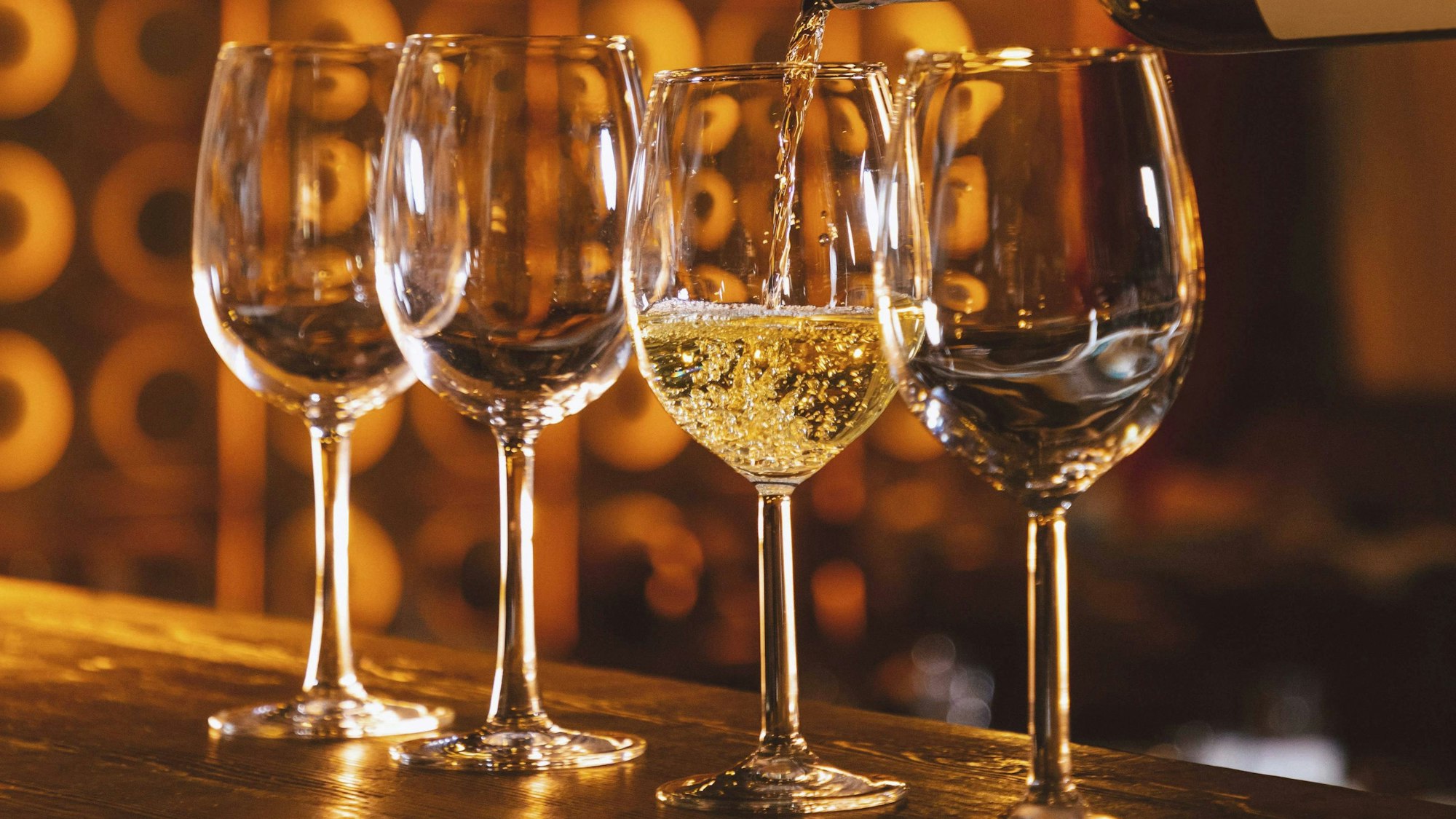 Barkeeper gießt Weißwein aus einer Flasche in eine Reihe von Gläsern auf einem Bartresen