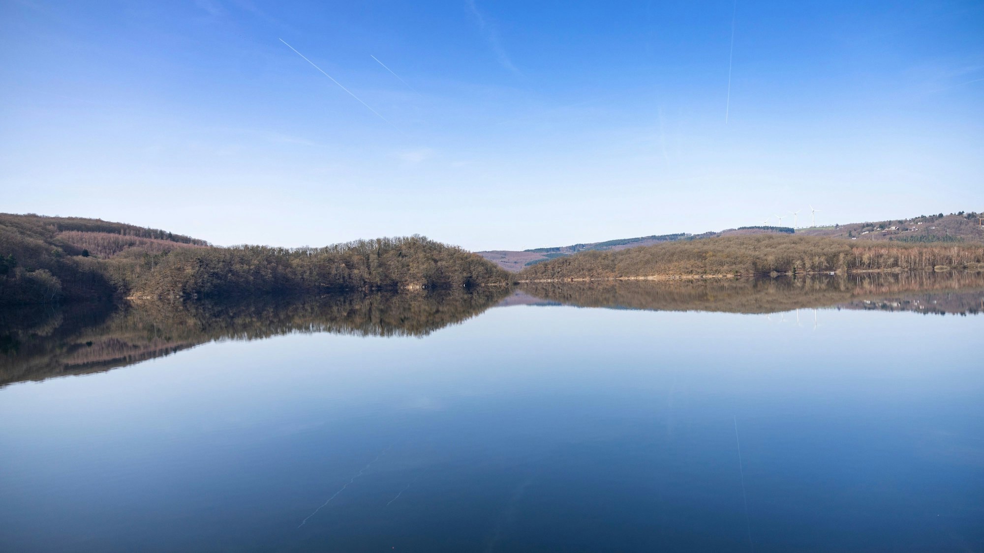 Blick auf den stillen Rursee im März, in dem sich der blaue Himmel spiegelt.