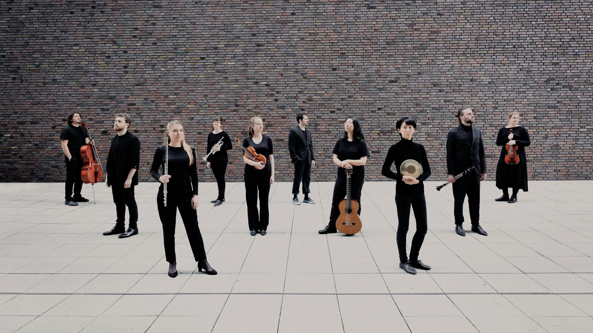 Musikerinnen und Musiker stehen, größtenteils mit Instrumenten in den Händen, nebeneinander.