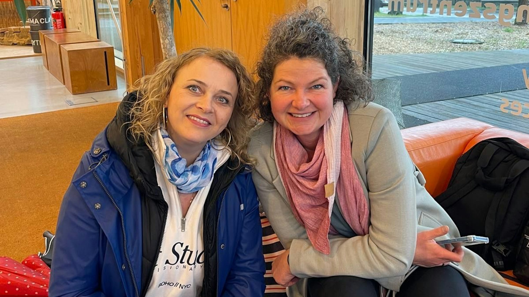 Zwei Frauen die auf einem Sofa sitzen und lächeln.