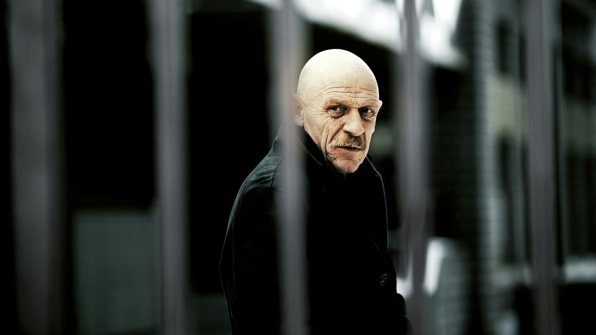 Das Bild zeigt Joe Bausch – im Vordergrund sind schwammig Gitterstäbe zu sehen.