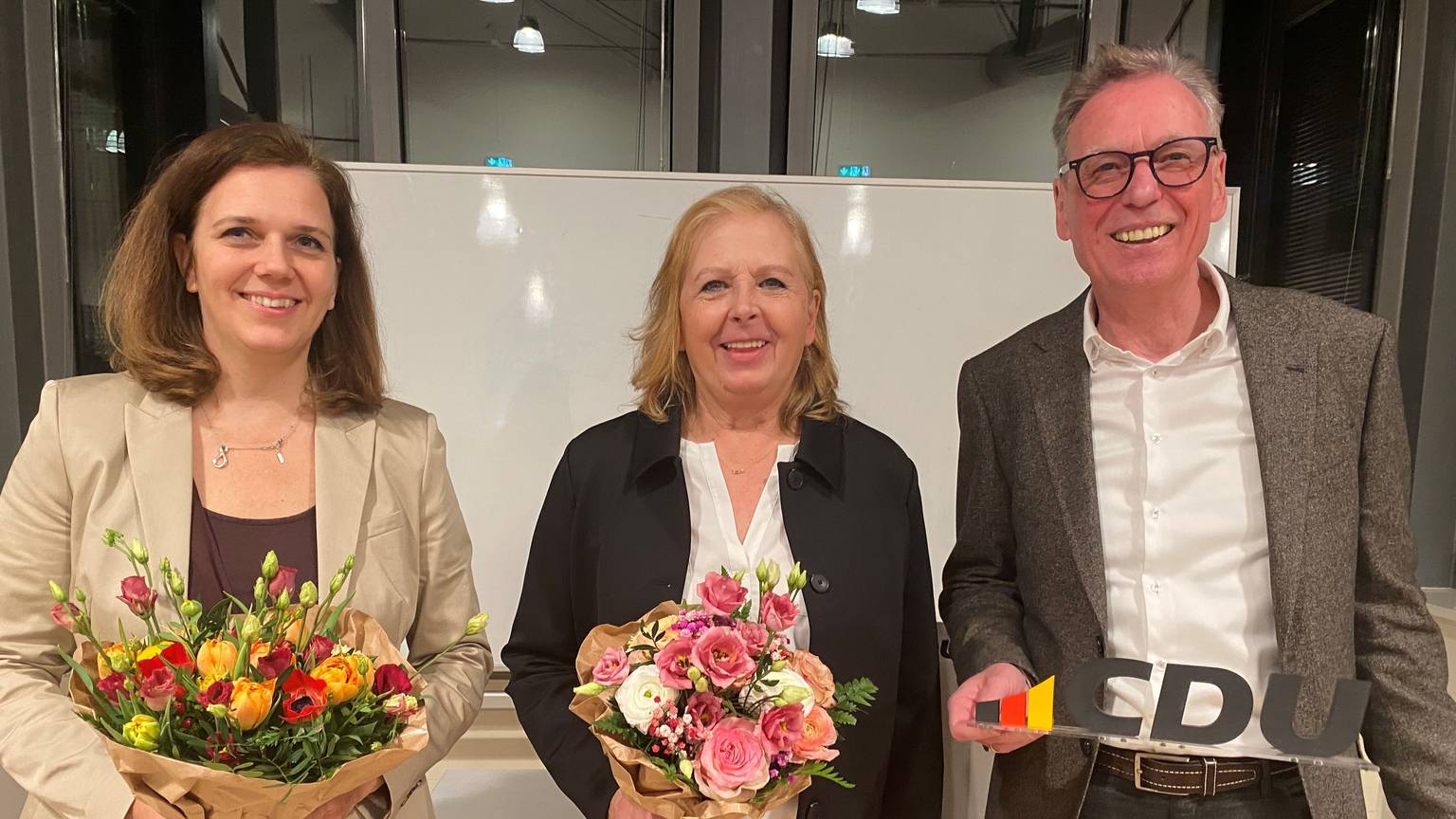 Zwei Frauen mit Blumensträußen und ein Mann mit einem kleinen CDU-Schild