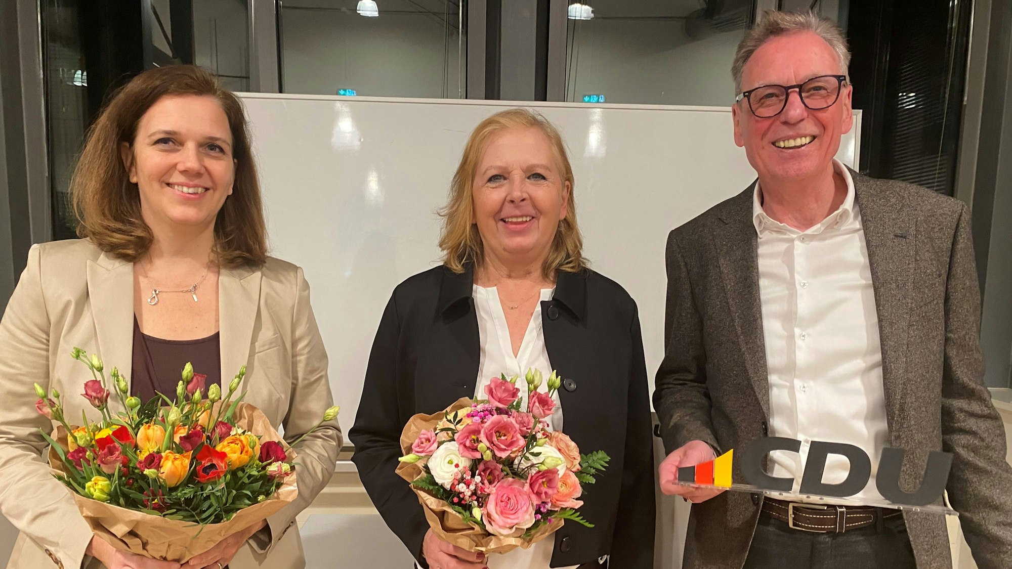 Zwei Frauen mit Blumensträußen und ein Mann mit einem kleinen CDU-Schild
