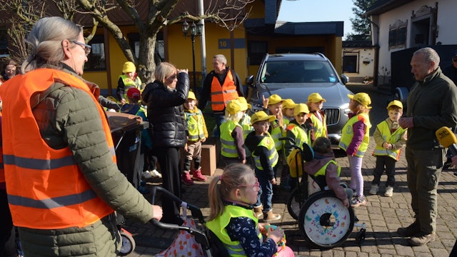 Kinder in Warnwesten und mit gelben Kappen, einige Kinder sitzen im Rollstuhl.