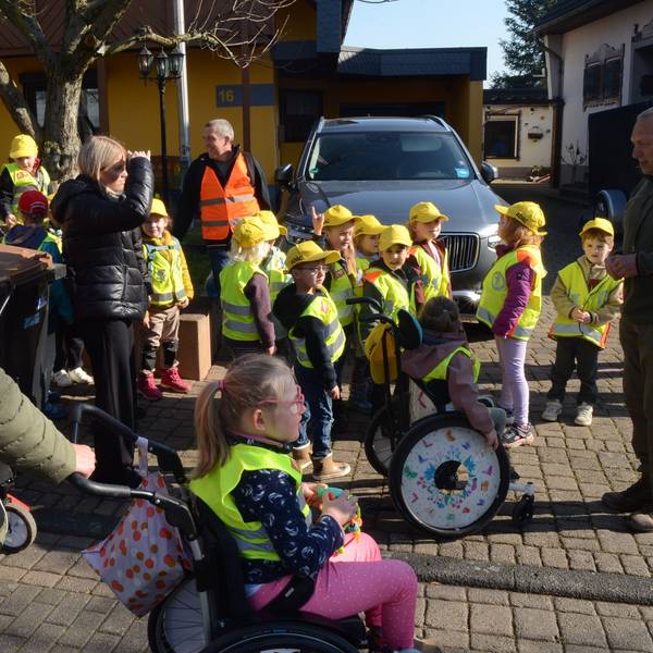 Kinder in Warnwesten und mit gelben Kappen, einige Kinder sitzen im Rollstuhl.