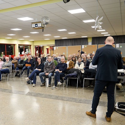 Die Aufnahme zeigt die sitzenden Teilnehmer in einem Saal der Gemünder Grundschule. Vor ihnen steht, von hinten fotografiert, Bürgermeister Ingo Pfennings.