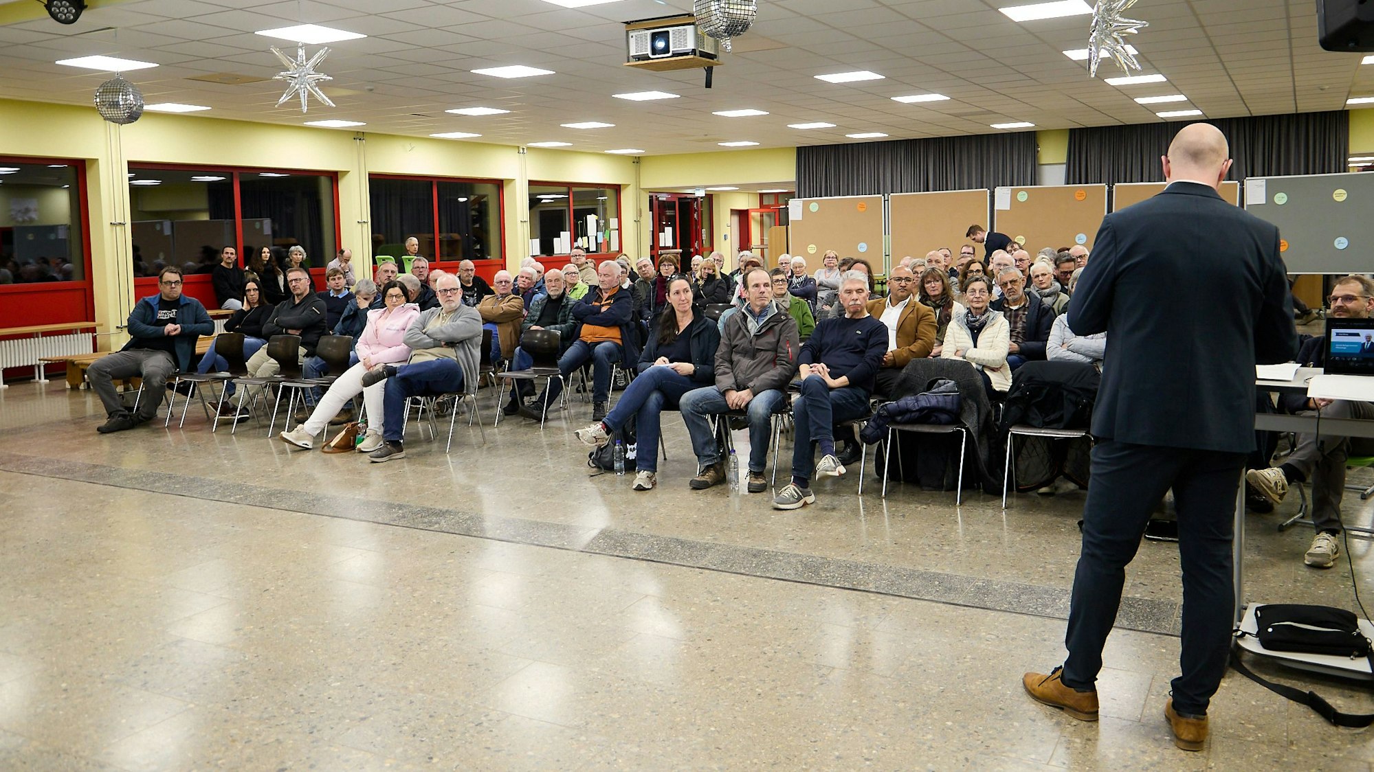 Die Aufnahme zeigt die sitzenden Teilnehmer in einem Saal der Gemünder Grundschule. Vor ihnen steht, von hinten fotografiert, Bürgermeister Ingo Pfennings.
