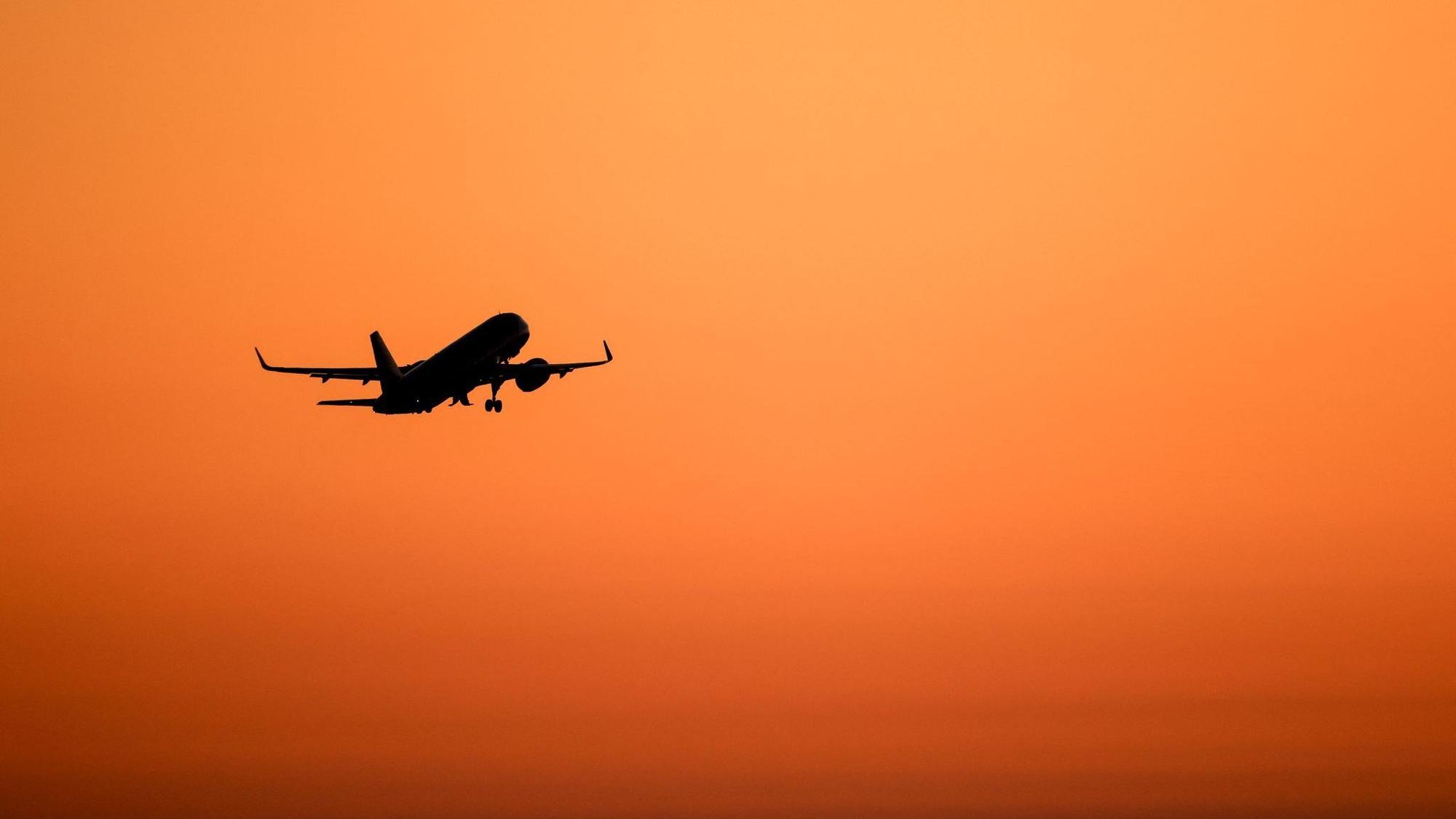 Ein Flugzeug hebt vor orangefarbenem Himmel ab