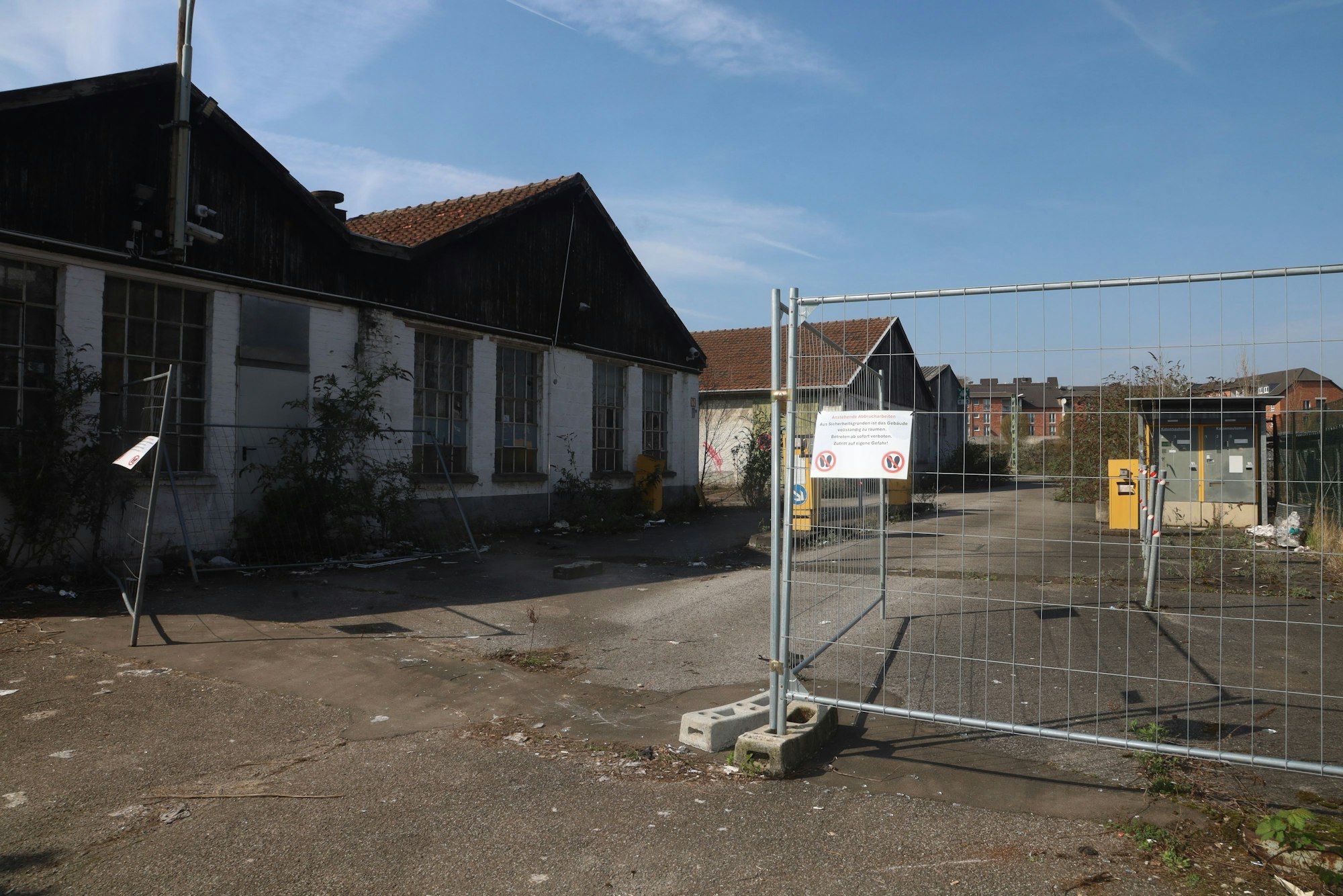 An einem Bauzaun prangt inzwischen ein Schild, das auf die Abbrucharbeiten hinweist. Vor dem Bauzaun sichert ein Eisentor das Gelände.