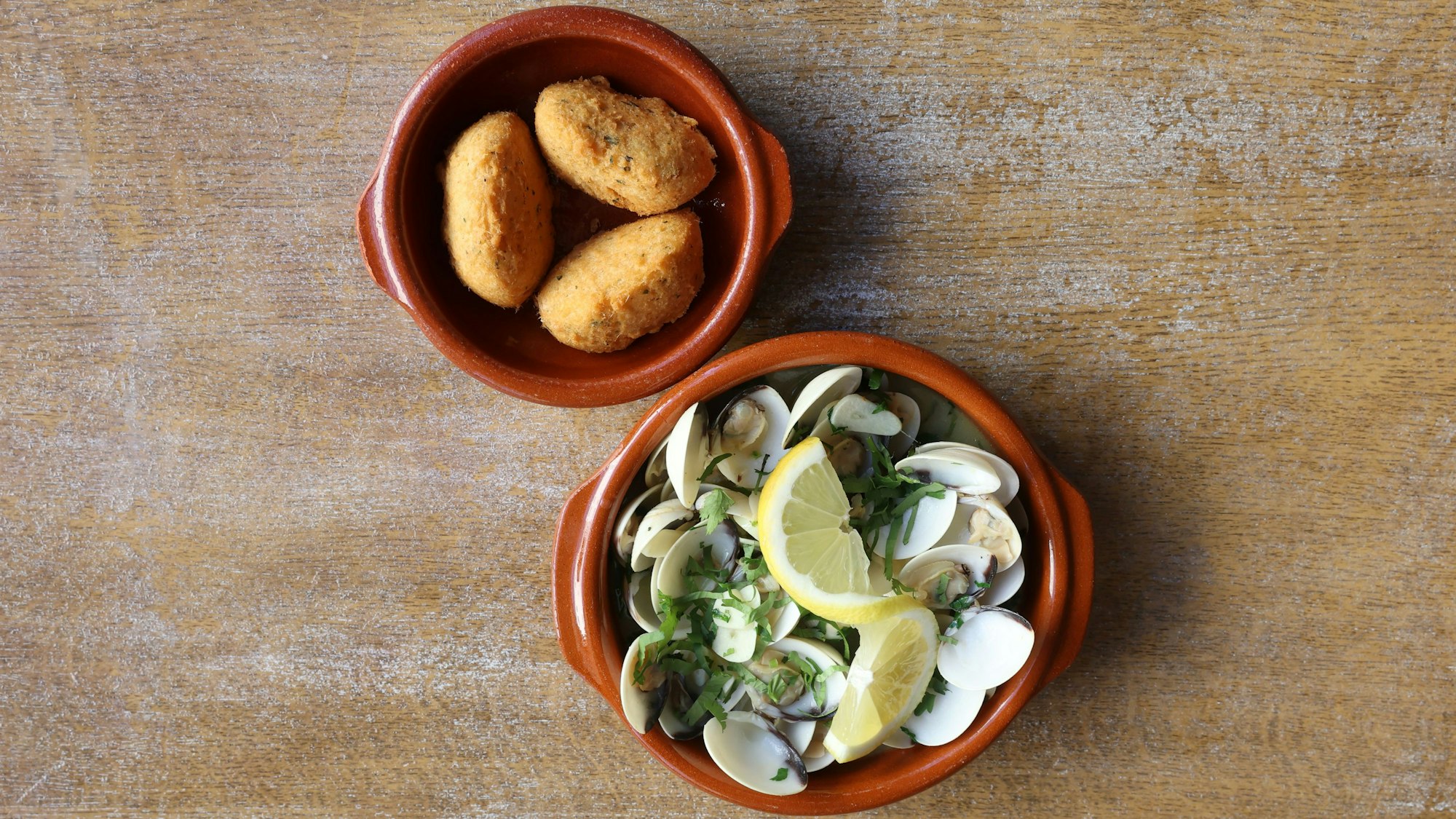 Zwei Tonschälchen sind zu sehen: eine mit Kroketten, eine mit Muscheln und Zitrone