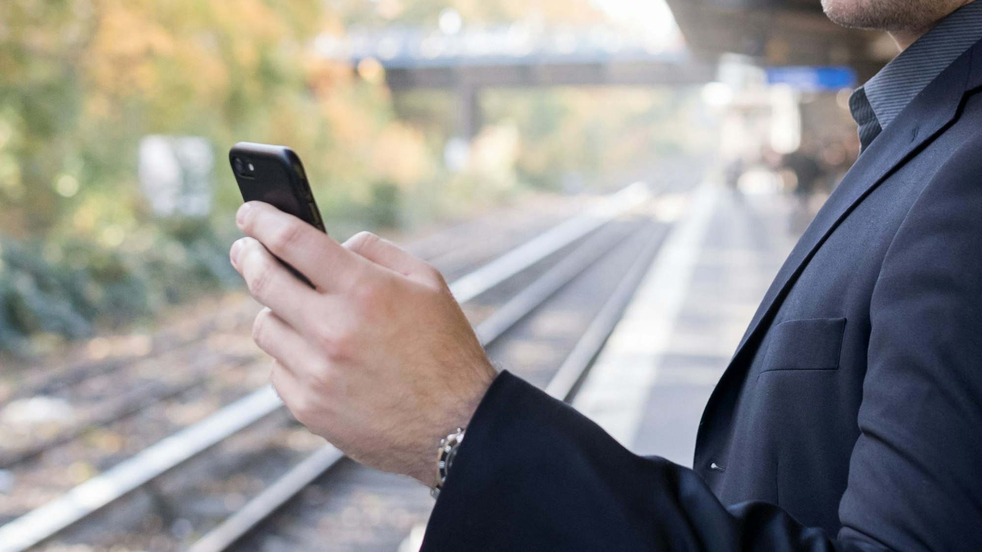 Mann mit Smartphone am Gleis