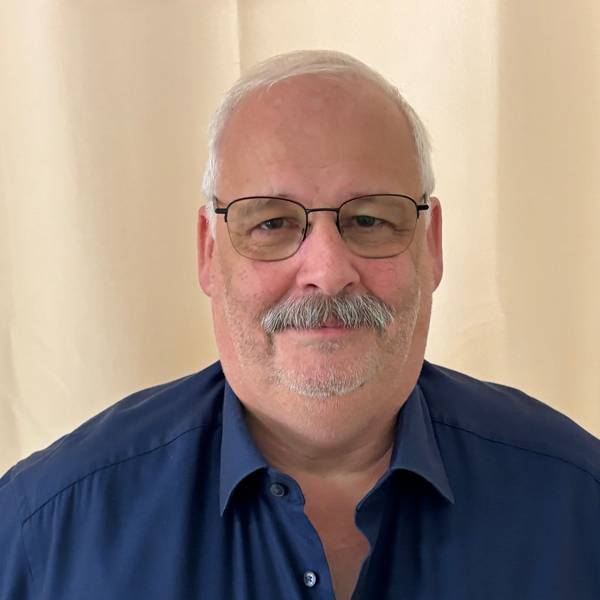 Auf dem Bild ist das Portrait eines Mannes mit Brille und in einem blauen Hemd zu sehen.