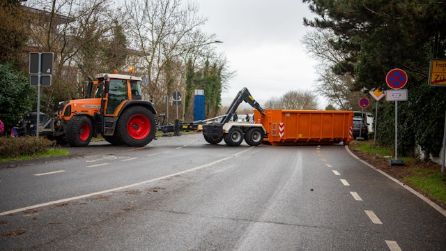 Ein Traktor setzt einen Container ab, um eine Zufahrtsstraße zum Zülpicher Karnevalszug zu sperren.