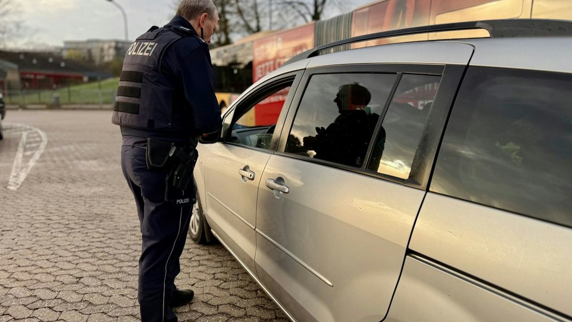 Ein Polizist oder eine Polizistin kontrolliert den Gurt eines Autofahrers oder einer Autofahrerin.